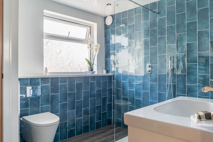 Luxury walk-in shower room with vibrant blue tiling, minimalist chrome fixtures, and a wall-hung toilet in a new house extension.